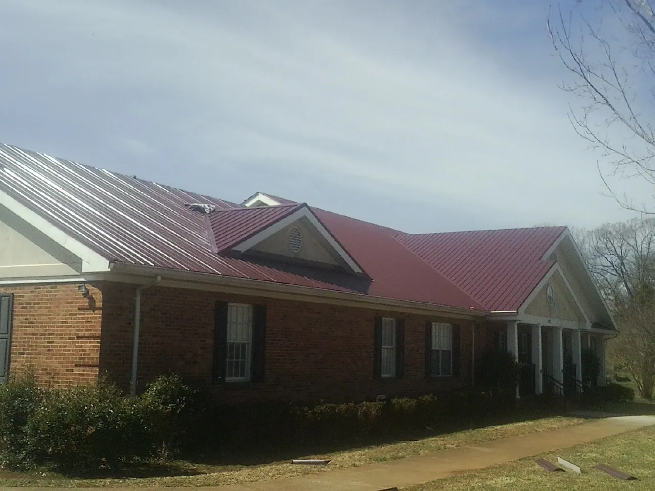 Red metal roof with gabled entries on a long brick building, from a Hail Damage Roof Repair job in Capitola