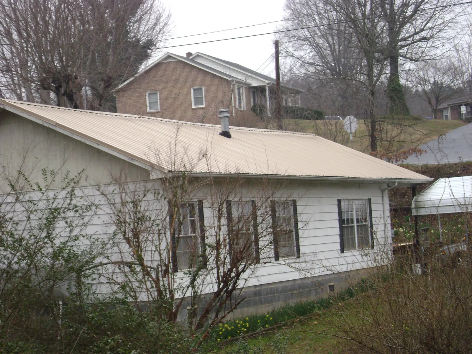 Tan metal roof on a white sided house set into a hillside — Commercial Roofing by Roofing Brothers in Capitola